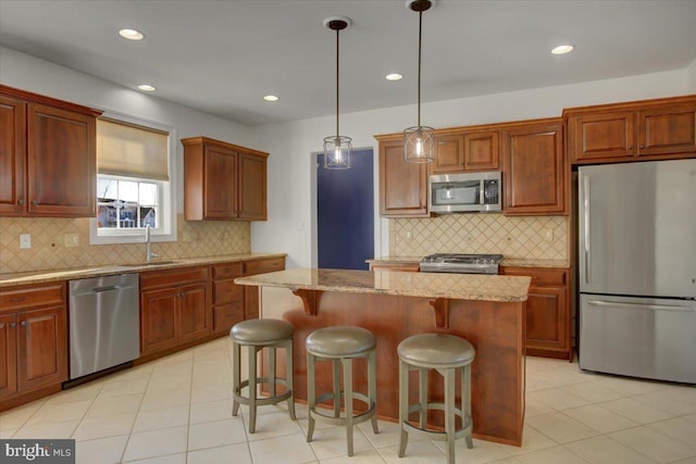 kitchen with light stone counters, appliances with stainless steel finishes, hanging light fixtures, and a kitchen island