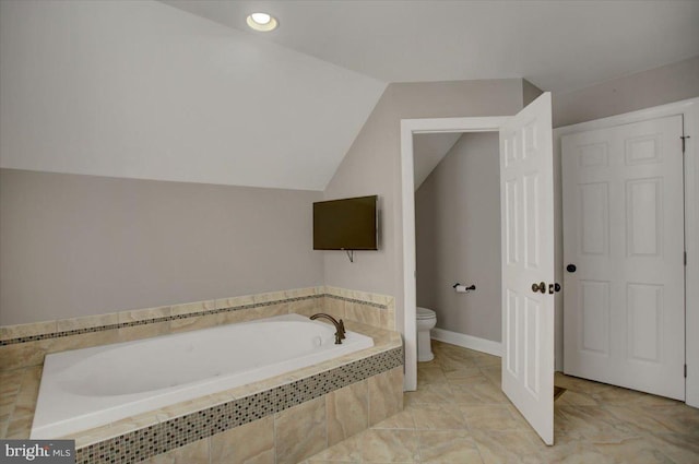 bathroom featuring lofted ceiling, toilet, and tiled bath