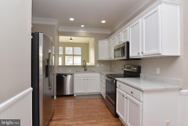 kitchen featuring appliances with stainless steel finishes, white cabinetry, sink, ornamental molding, and light stone counters