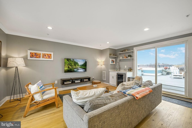 living room featuring light wood-type flooring, beverage cooler, ornamental molding, baseboards, and wet bar