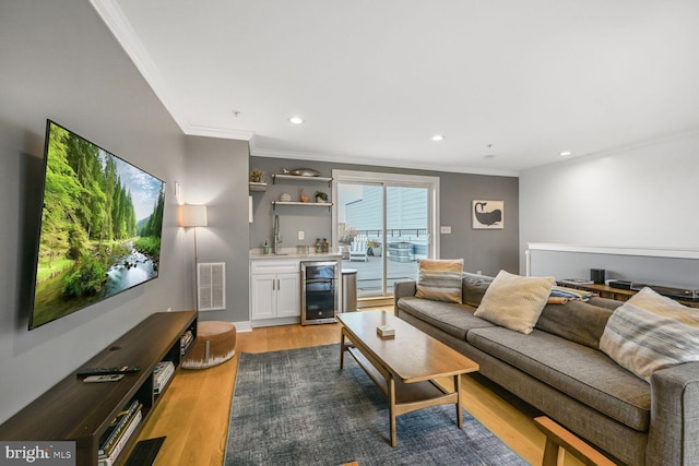 living area featuring wine cooler, light wood-style flooring, visible vents, and ornamental molding