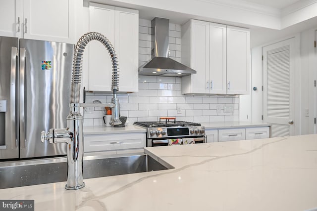 kitchen with ornamental molding, white cabinets, appliances with stainless steel finishes, wall chimney range hood, and tasteful backsplash