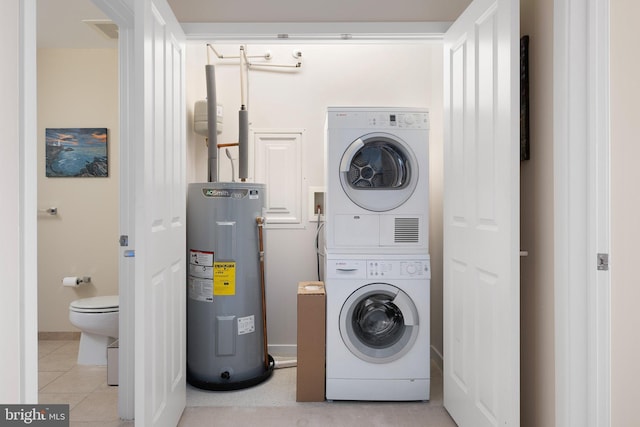 washroom featuring stacked washer / drying machine, electric water heater, and light tile patterned flooring