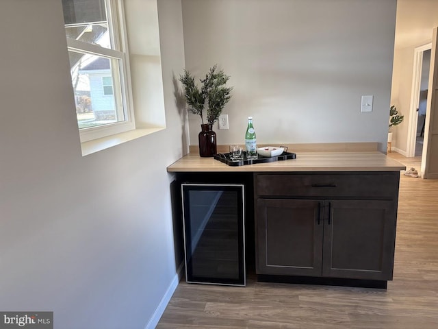 bar with beverage cooler, dark brown cabinets, and light hardwood / wood-style flooring