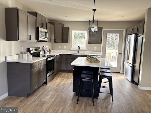 kitchen with sink, appliances with stainless steel finishes, dark brown cabinets, a kitchen island, and a kitchen bar