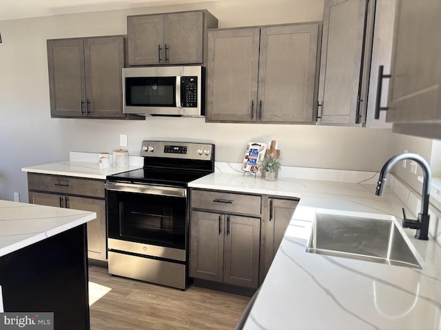 kitchen with dark brown cabinetry, sink, stainless steel appliances, light stone countertops, and light hardwood / wood-style floors