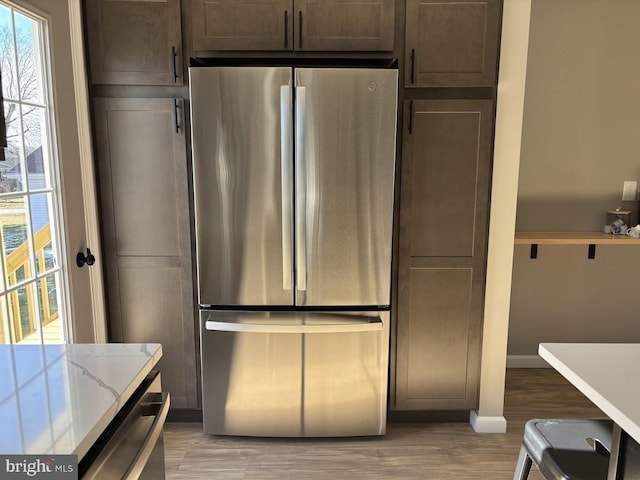 kitchen with appliances with stainless steel finishes, dark brown cabinets, light stone counters, and light wood-type flooring