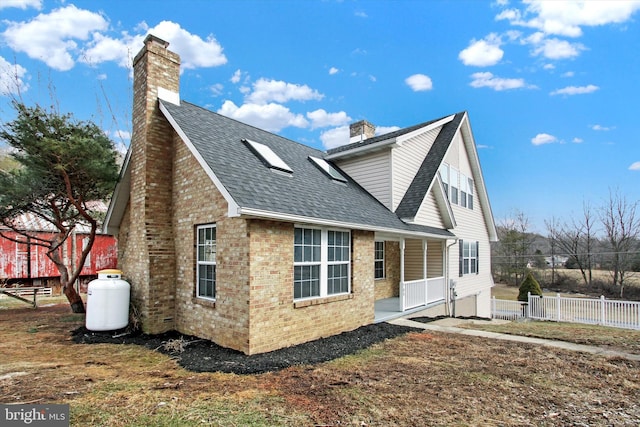 exterior space with a shingled roof, brick siding, fence, and a chimney