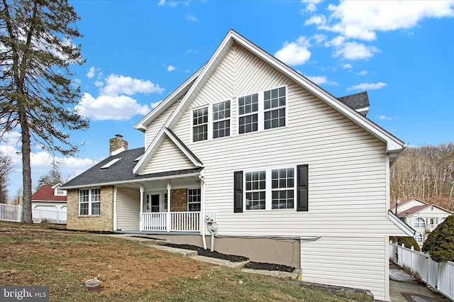 back of property with brick siding, a yard, a chimney, covered porch, and fence