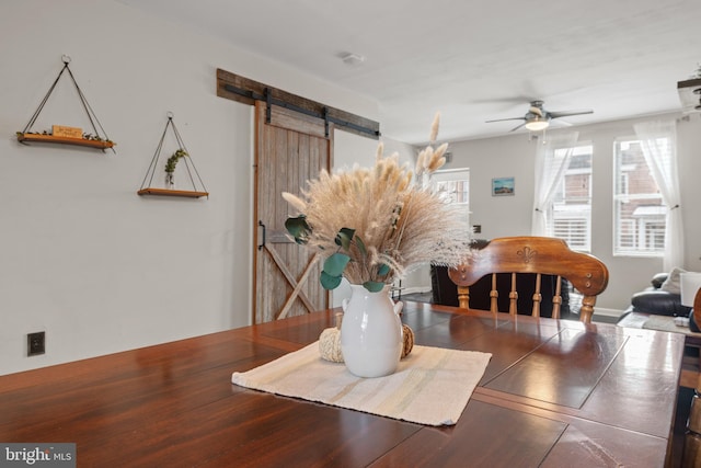 dining space with ceiling fan and a barn door