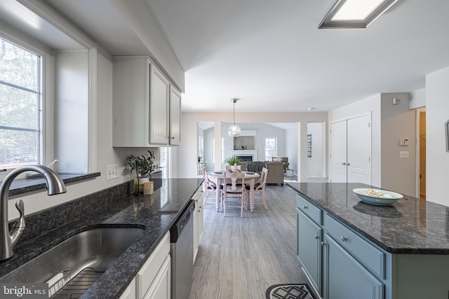 kitchen with pendant lighting, sink, dark stone countertops, stainless steel dishwasher, and light hardwood / wood-style flooring