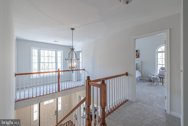 corridor with a chandelier, carpet, and a wealth of natural light