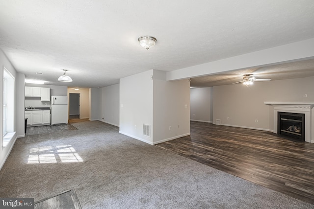 unfurnished living room featuring ceiling fan, dark carpet, and a textured ceiling