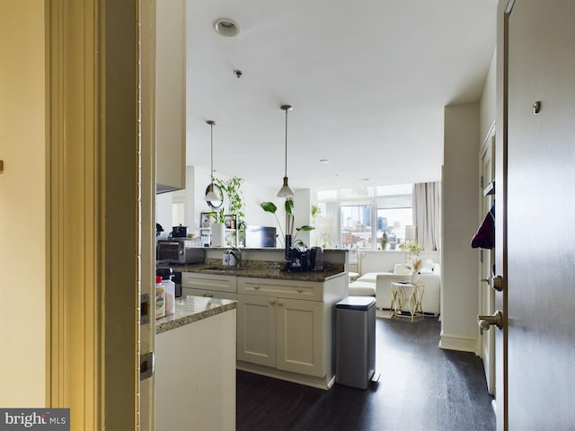 kitchen with white cabinetry, decorative light fixtures, dark hardwood / wood-style floors, kitchen peninsula, and dark stone counters