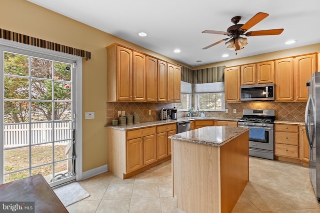 kitchen with sink, a center island, light tile patterned floors, appliances with stainless steel finishes, and light stone countertops