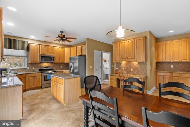 kitchen with pendant lighting, sink, stainless steel appliances, a center island, and light stone countertops