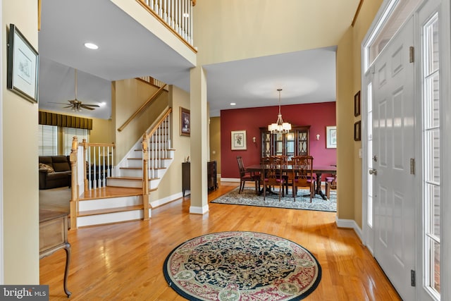 foyer featuring hardwood / wood-style flooring, ceiling fan with notable chandelier, and a high ceiling