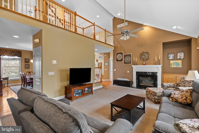 carpeted living room with a premium fireplace, ceiling fan, and high vaulted ceiling