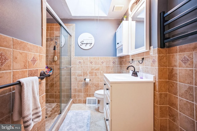 bathroom with toilet, a skylight, tile walls, vanity, and a shower with door