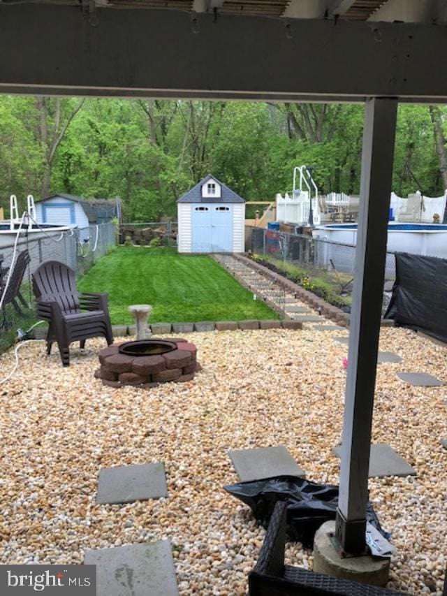 view of yard featuring a storage unit, an empty pool, and an outdoor fire pit