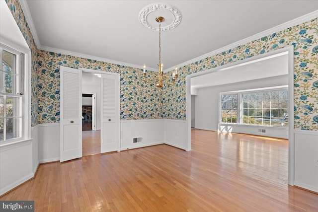 unfurnished dining area with hardwood / wood-style floors, crown molding, and a notable chandelier