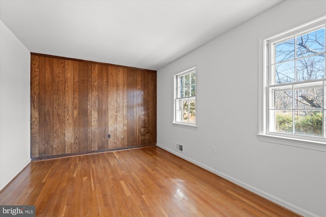 empty room featuring wooden walls, a wealth of natural light, and light hardwood / wood-style flooring