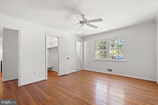 unfurnished bedroom with hardwood / wood-style floors, crown molding, a walk in closet, and ceiling fan