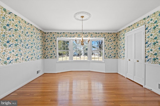 unfurnished dining area featuring ornamental molding, a notable chandelier, and wood-type flooring