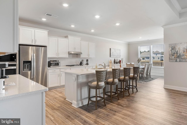 kitchen featuring a breakfast bar, a kitchen island with sink, stainless steel appliances, ornamental molding, and white cabinets