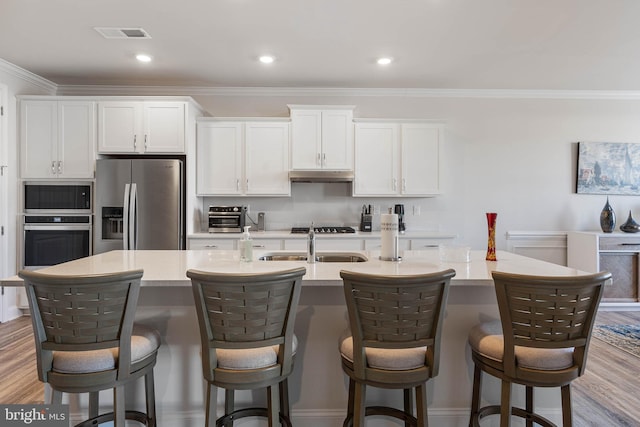 kitchen with stainless steel appliances, an island with sink, wood-type flooring, and white cabinets