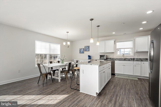 kitchen with stainless steel appliances, a center island, light stone countertops, white cabinets, and decorative light fixtures