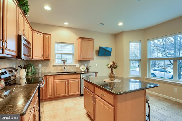 kitchen featuring stainless steel appliances, a center island, sink, and dark stone counters