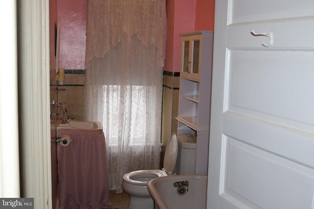 bathroom featuring sink, tile walls, a bathtub, and toilet