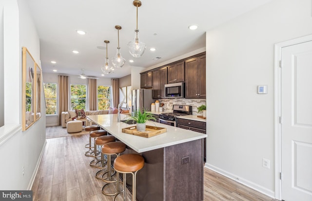 kitchen featuring pendant lighting, a breakfast bar, stainless steel appliances, dark brown cabinetry, and a center island with sink