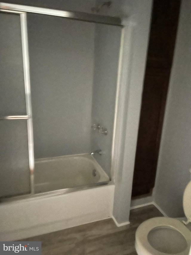 bathroom featuring wood-type flooring, washtub / shower combination, and toilet