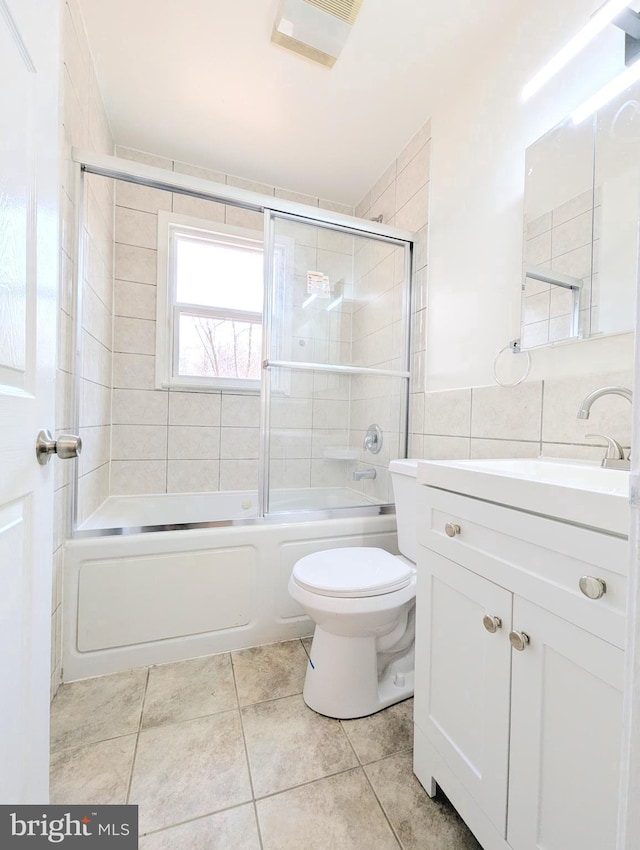 full bathroom featuring combined bath / shower with glass door, tile walls, tile patterned flooring, vanity, and toilet