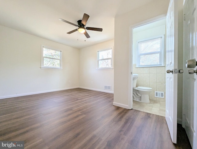 unfurnished bedroom with dark wood-type flooring, connected bathroom, and multiple windows