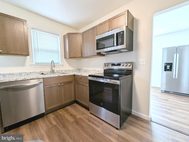 kitchen with hardwood / wood-style flooring, stainless steel appliances, light stone countertops, and sink