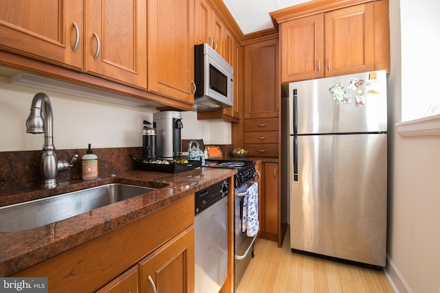 kitchen featuring light wood-type flooring, stainless steel appliances, sink, and dark stone counters