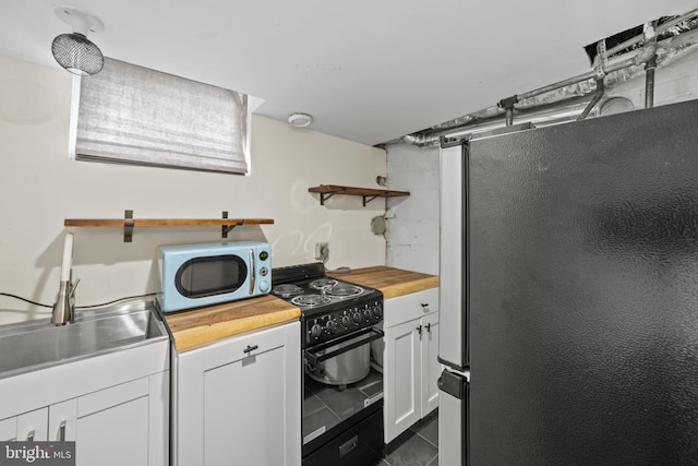 kitchen with butcher block countertops, stainless steel fridge, dark tile patterned floors, white cabinets, and black / electric stove