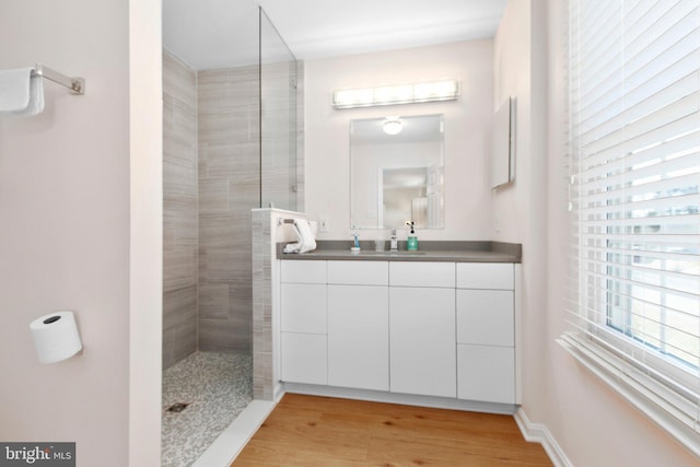 full bathroom featuring a walk in shower, vanity, baseboards, and wood finished floors