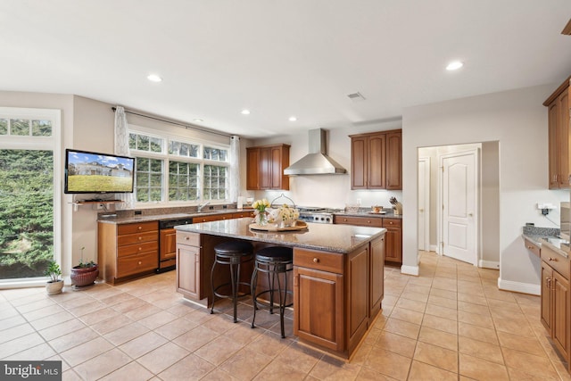 kitchen featuring wall chimney exhaust hood, sink, a kitchen island, stone counters, and stove