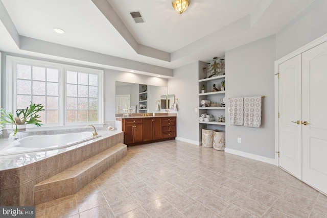 bathroom featuring vanity, tiled tub, built in features, and a raised ceiling