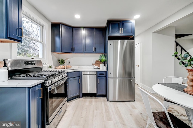 kitchen featuring blue cabinets, appliances with stainless steel finishes, sink, and light wood-type flooring