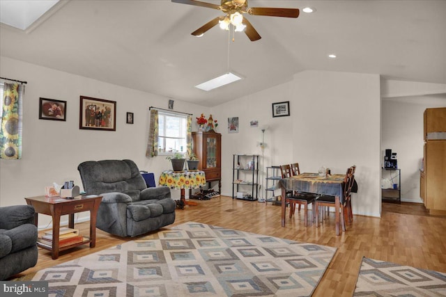 living room with hardwood / wood-style floors, vaulted ceiling with skylight, and ceiling fan