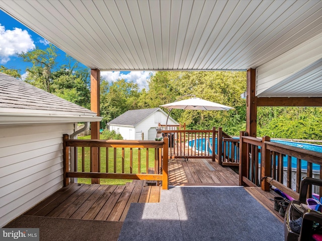 wooden deck featuring a pool, an outbuilding, and a lawn