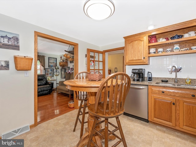 kitchen with tasteful backsplash, stainless steel dishwasher, sink, and dark stone countertops