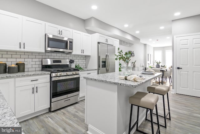 kitchen featuring light stone counters, stainless steel appliances, a center island, and white cabinets