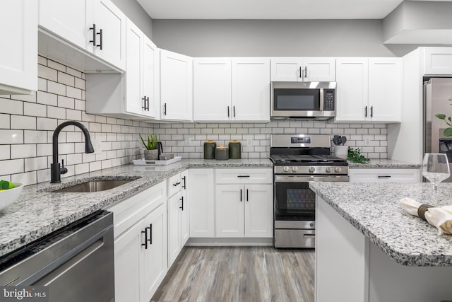 kitchen featuring sink, backsplash, white cabinets, light hardwood / wood-style floors, and stainless steel appliances