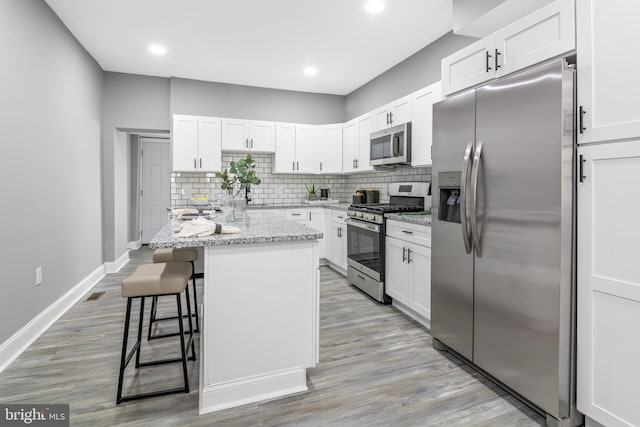 kitchen with appliances with stainless steel finishes, white cabinetry, a kitchen island, light stone countertops, and a kitchen bar